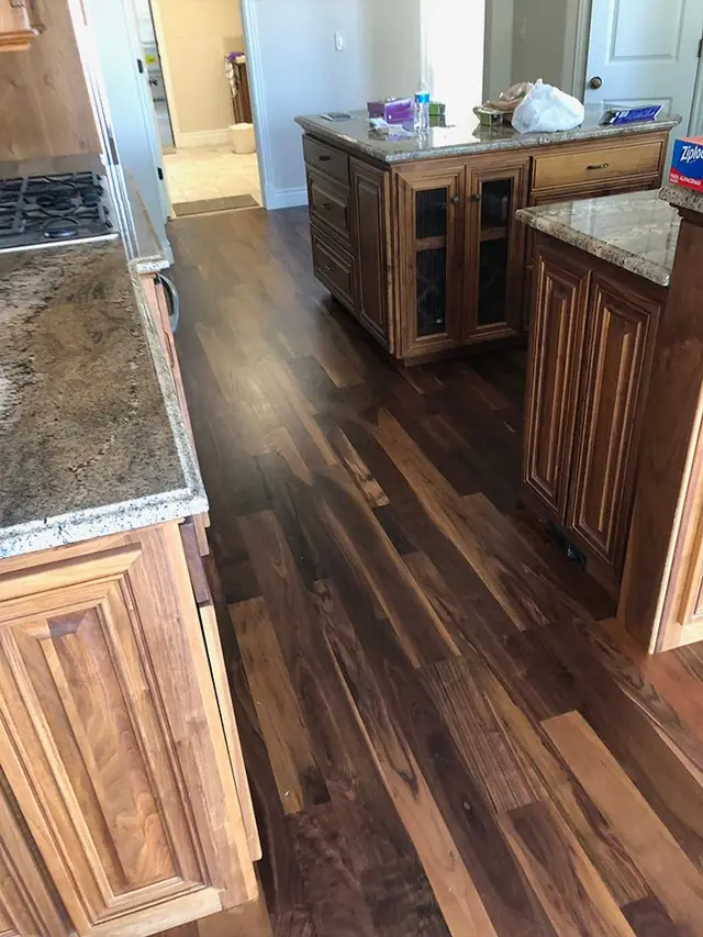 Dark-toned hardwood floor running into a kitchen with granite counters and wood cabinets