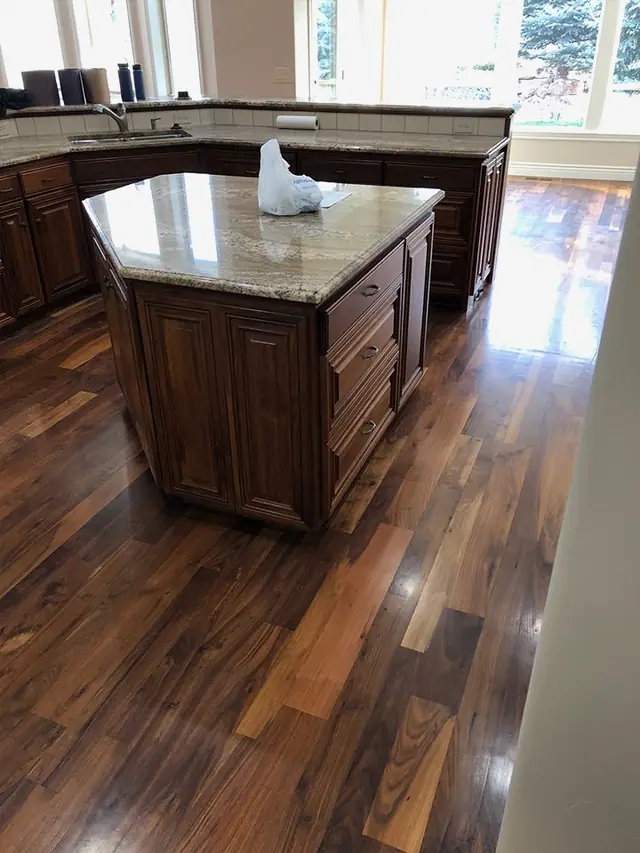 Dark stained hardwood floor beside a granite kitchen island in window light